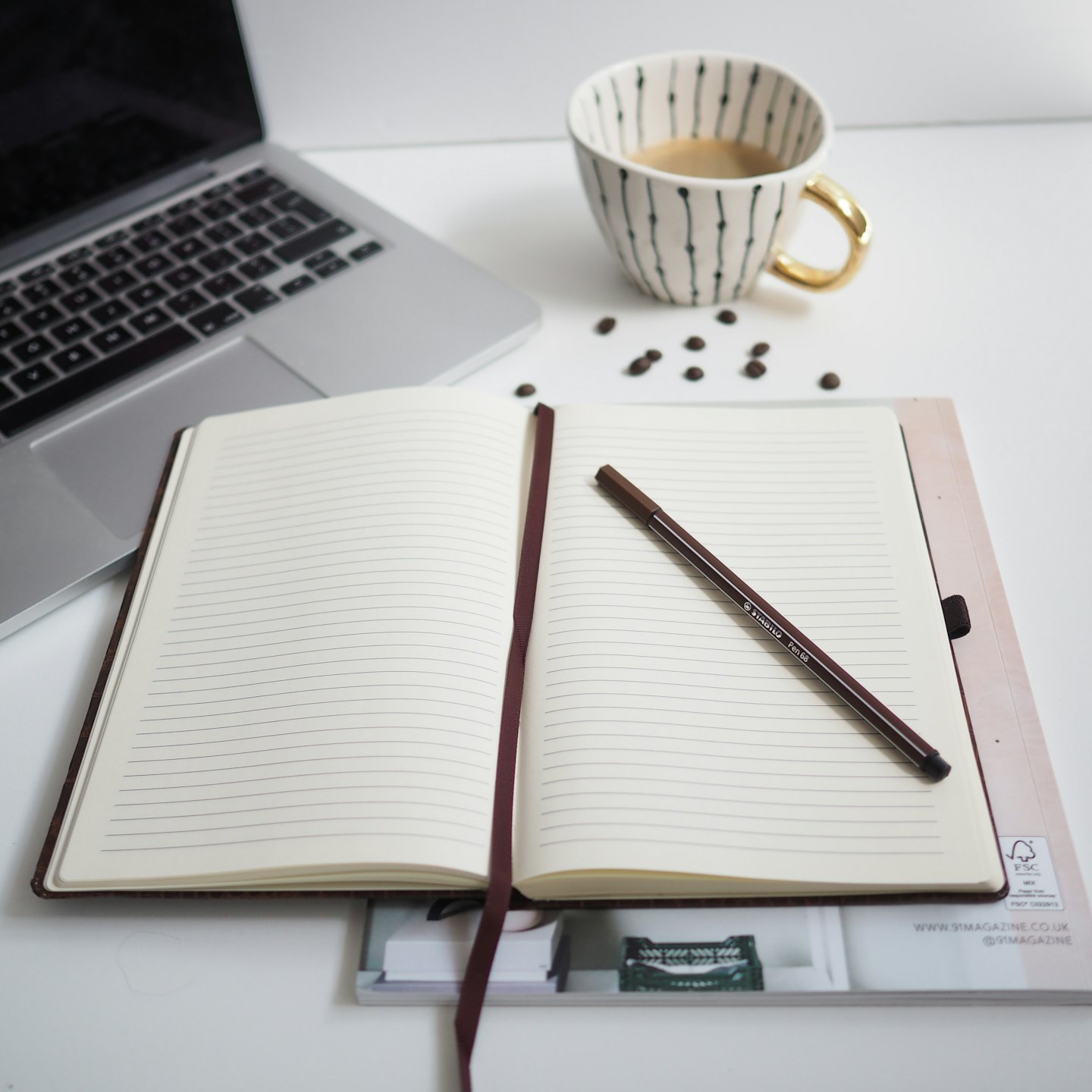 Vista dall'alto di una scrivania minimalista con laptop, taccuino e tazza di caffè.